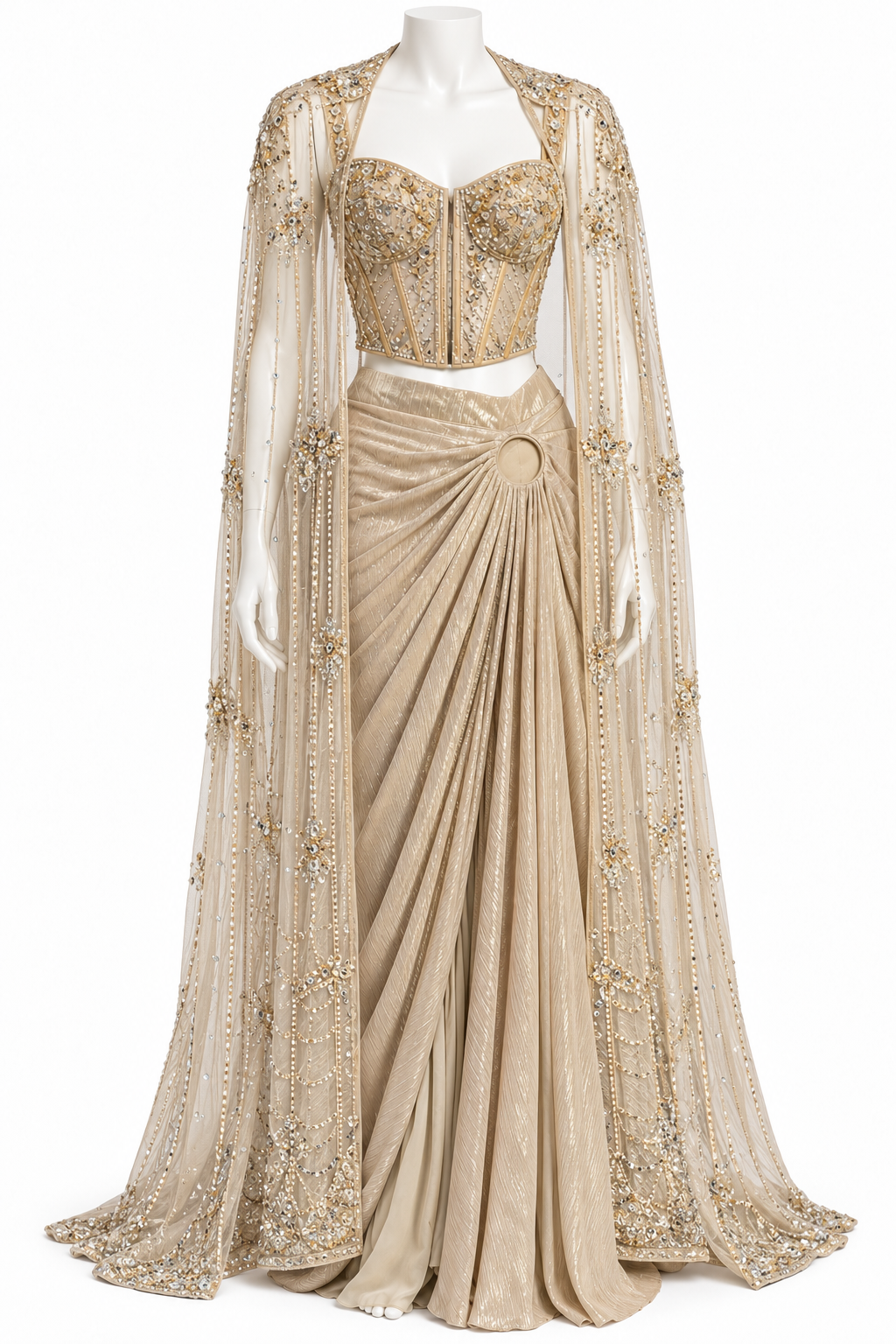 A beige and gold two-piece traditional outfit displayed on a mannequin, featuring a heavily embellished embroidered crop top and a draped pleated skirt with a matching sheer embroidered cape.