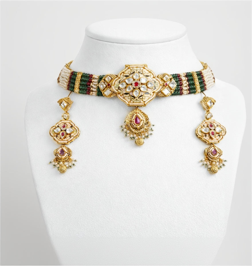 Gold necklace with green and red accents on a white mannequin bust.