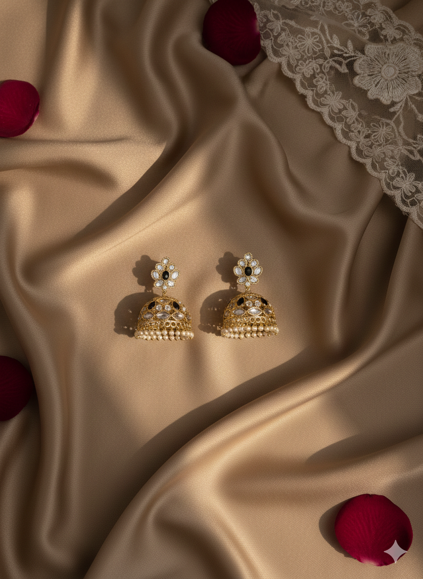 Gold earrings with floral designs on a beige fabric background with red rose petals.