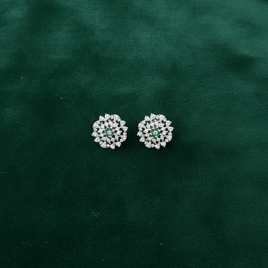 Pair of silver earrings with green gemstones on a dark green fabric background