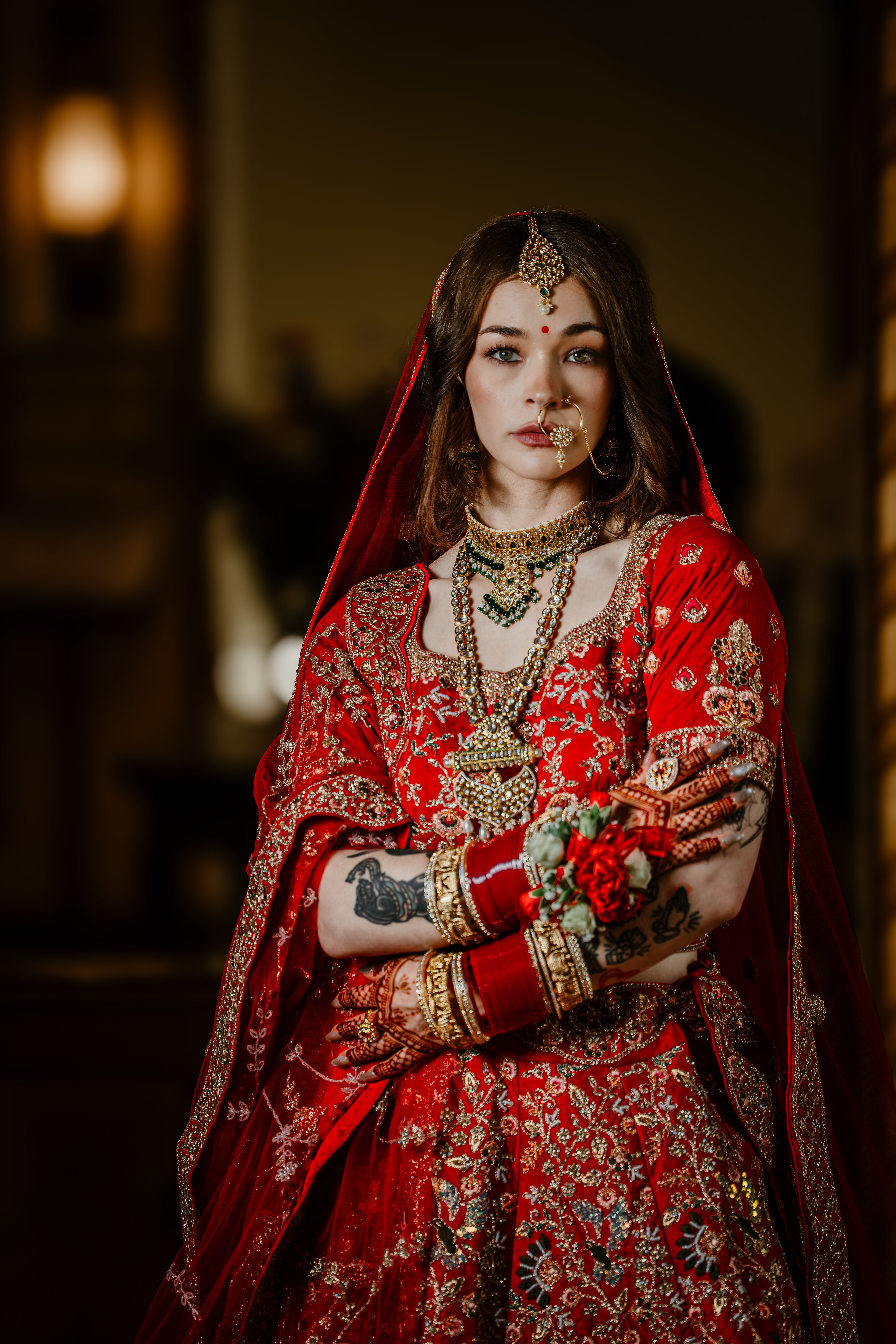 Woman in traditional red bridal outfit with gold jewelry and floral decorations.