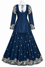 A navy blue traditional long dress displayed on a white mannequin against a white background. The dress features a fitted bodice with a tie-back neckline, three-quarter sleeves with floral embroidery at the cuffs, and a pleated skirt decorated with small colorful embroidered dots and a wide floral border at the hem.