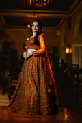 Woman in traditional orange and red embroidered outfit standing in a dimly lit room.