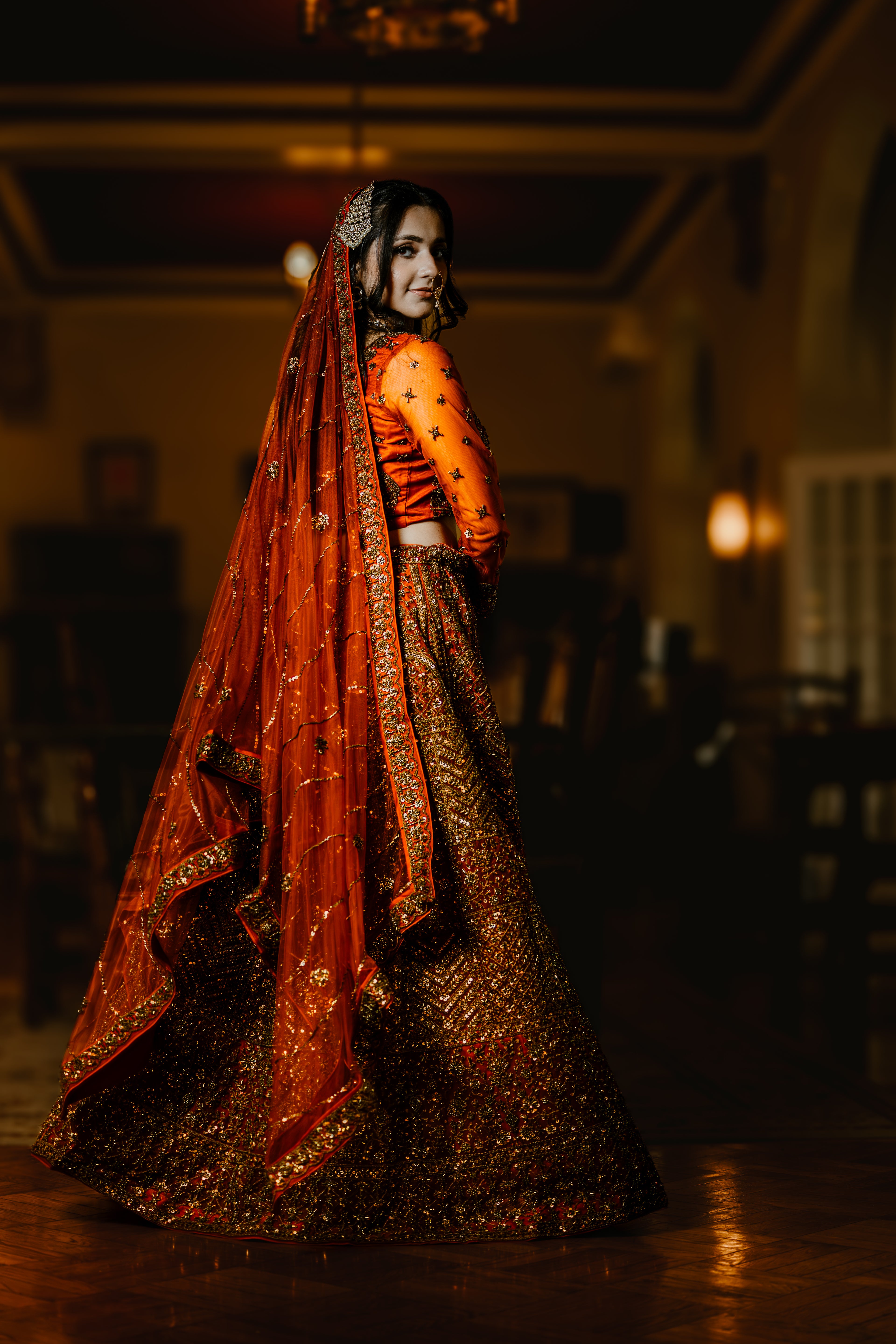 Woman in traditional orange and gold embroidered outfit in a dimly lit room.