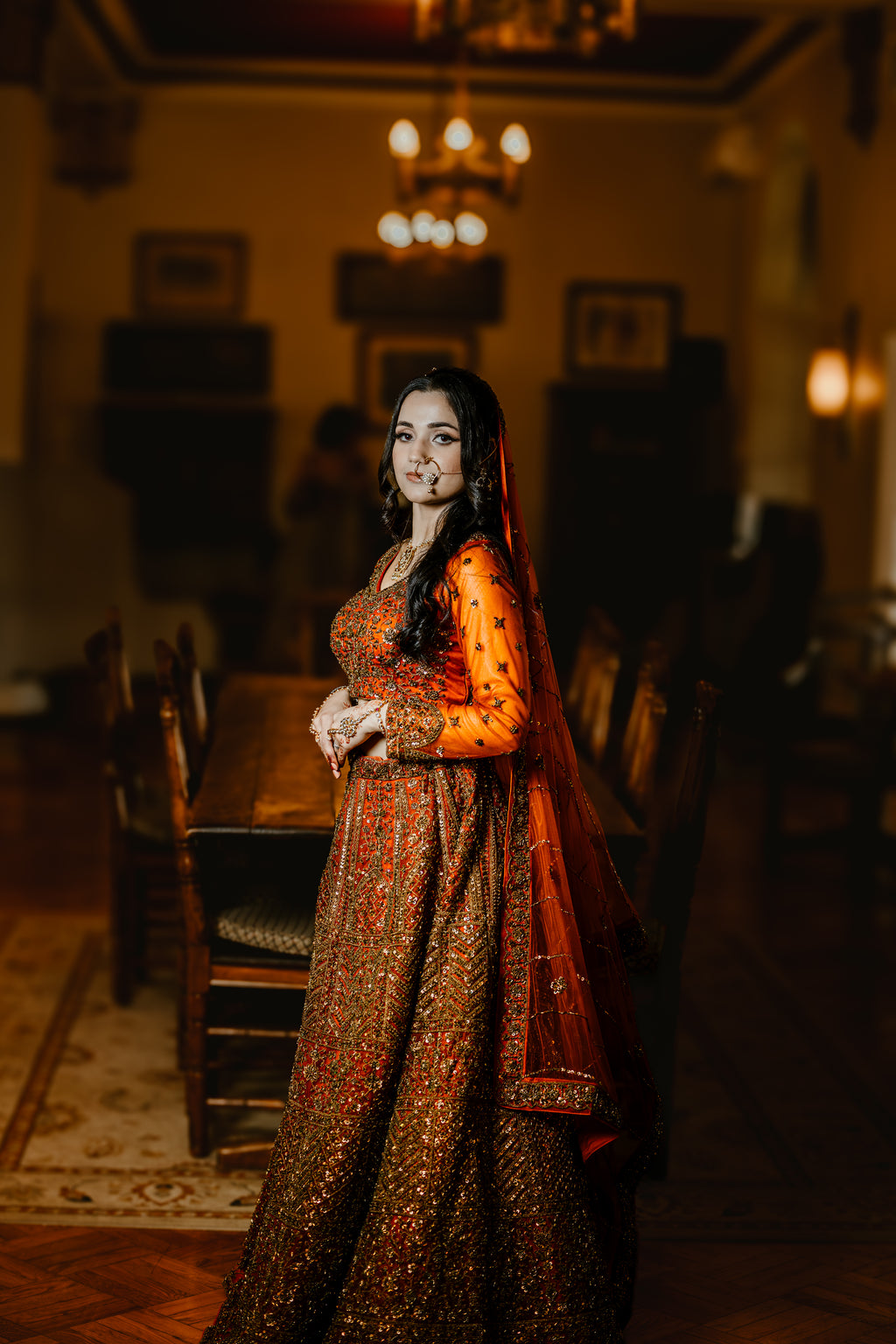 Woman in traditional attire standing in a dimly lit room with wooden furniture.