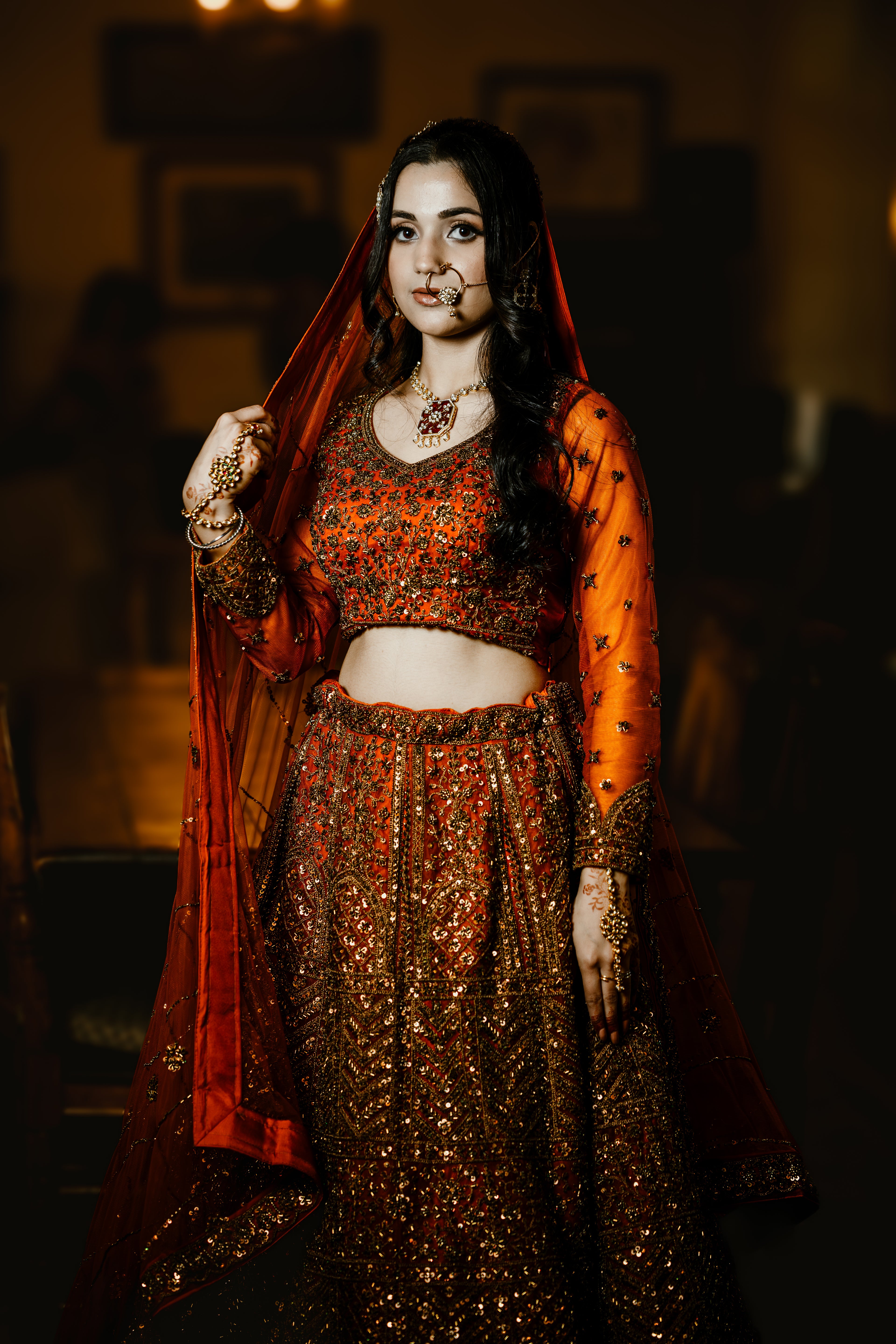 Woman in traditional orange and red outfit with dupatta, blurred background