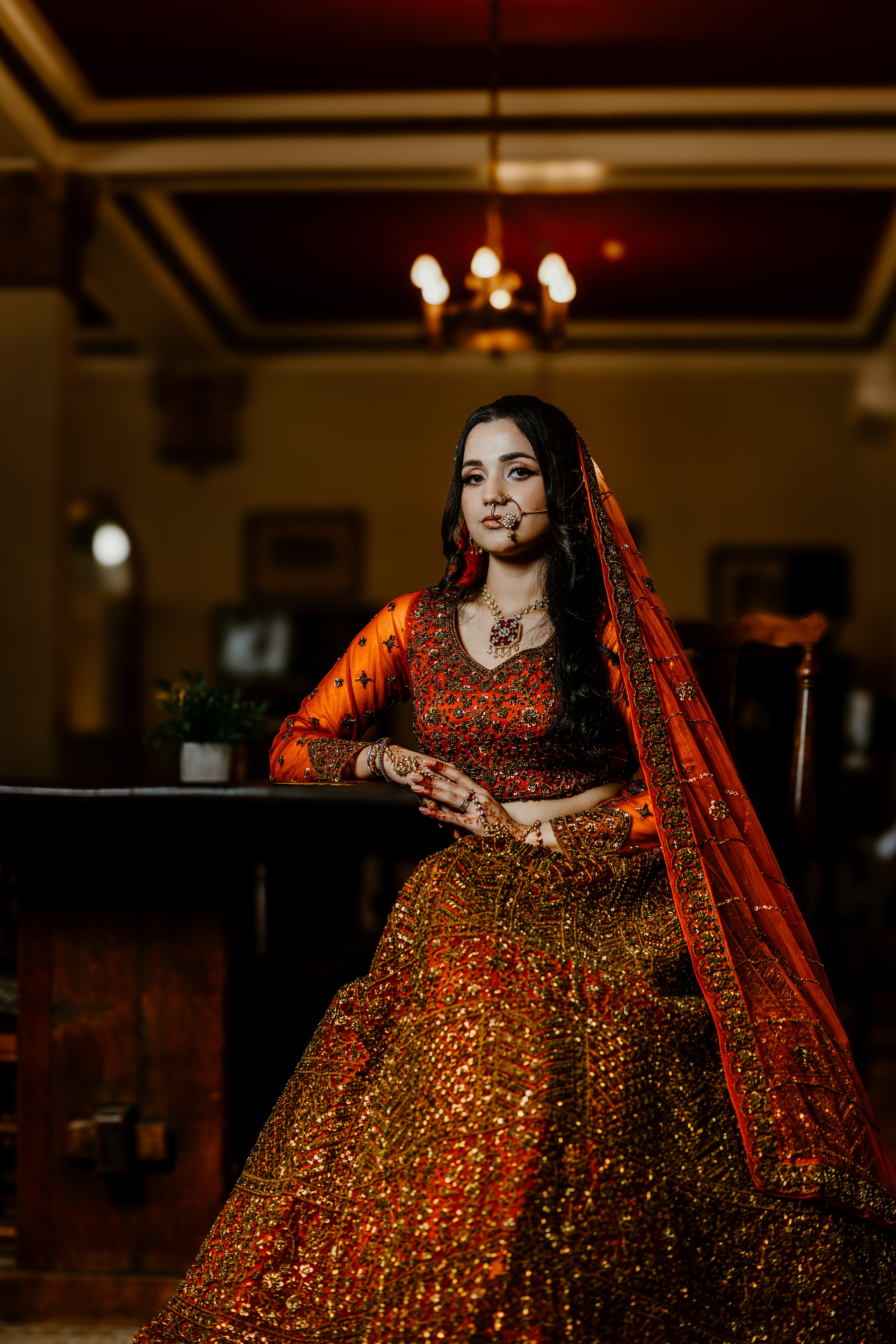 Woman in traditional orange and gold outfit with a red dupatta in an indoor setting