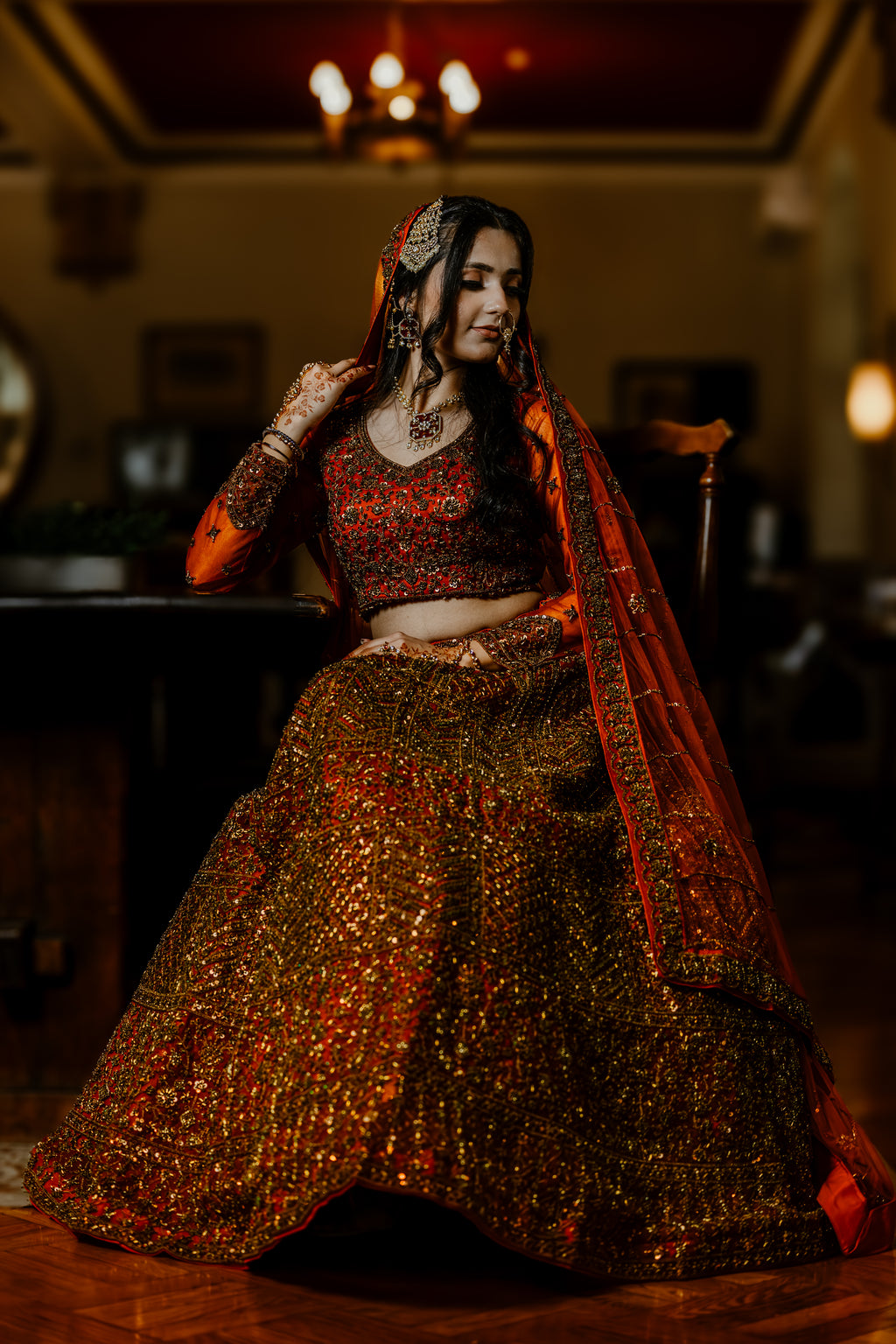 Woman in traditional red and gold outfit with intricate jewelry indoors.