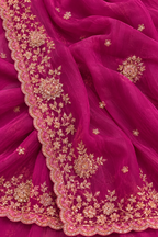 A close-up of a magenta pink dupatta or fabric with intricate gold floral embroidery and scalloped borders.