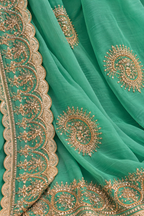 A close-up of a mint green fabric, likely a saree or dupatta, featuring detailed gold zari embroidery and scalloped borders.