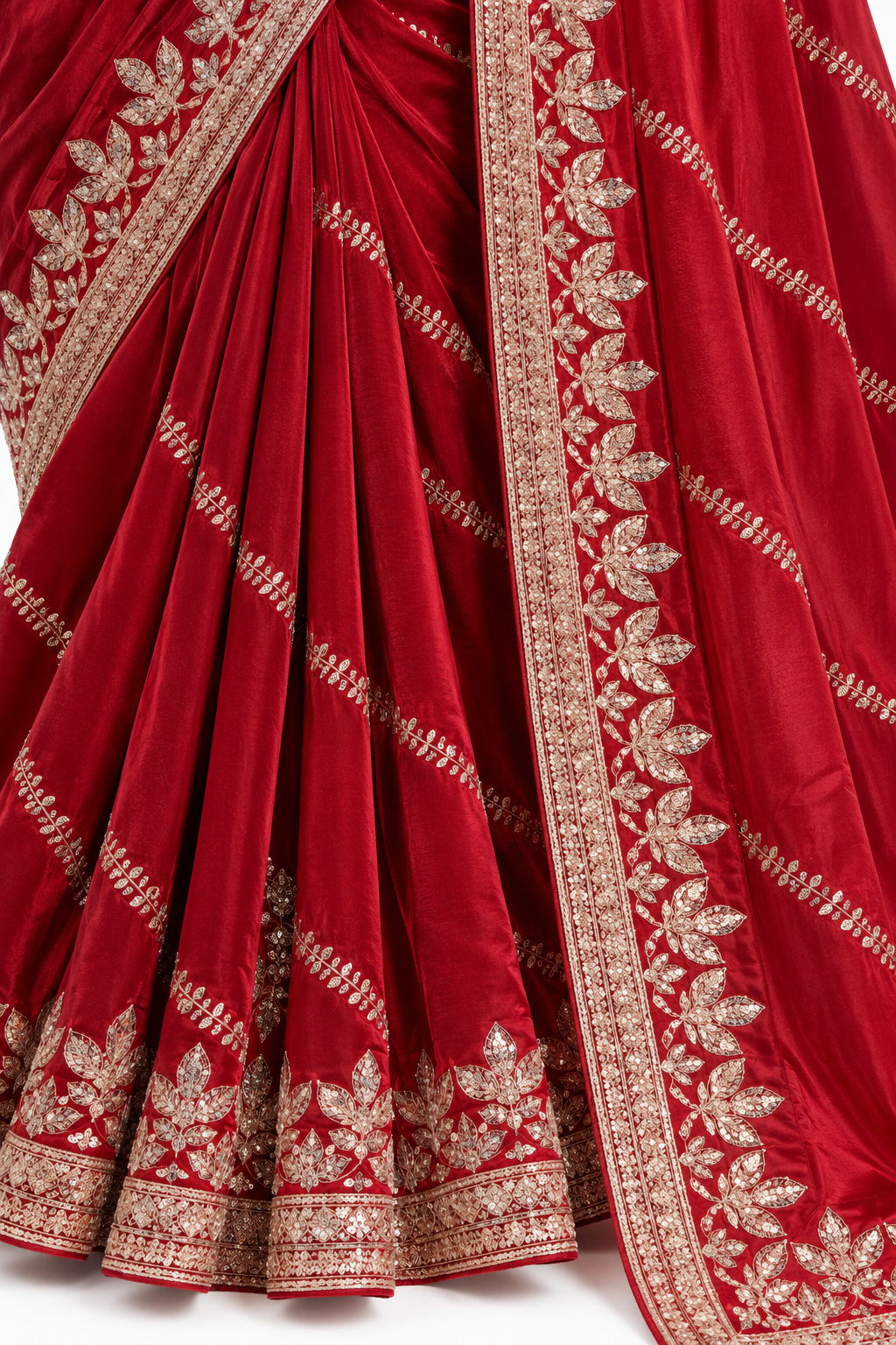 A close-up of a deep red silk saree with intricate gold zari embroidery, showing the pleated body and the border design.