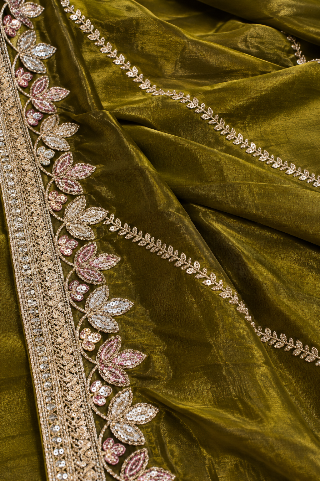 Close-up of an olive green fabric with ornate metallic embroidered borders and pink crystal leaf motifs.