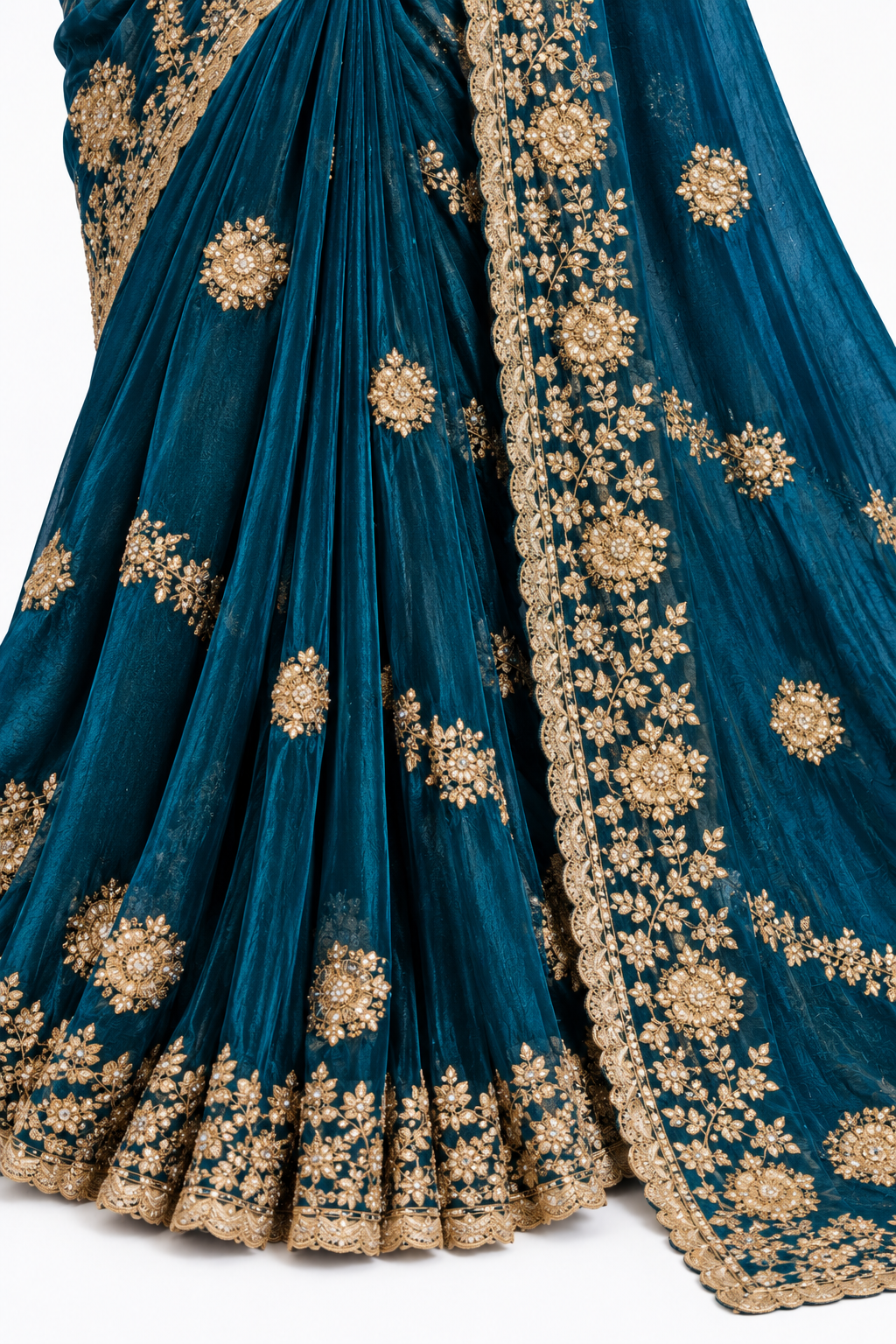A close-up of a teal blue georgette saree with intricate gold floral embroidery and a wide gold border, shown against a plain white background.