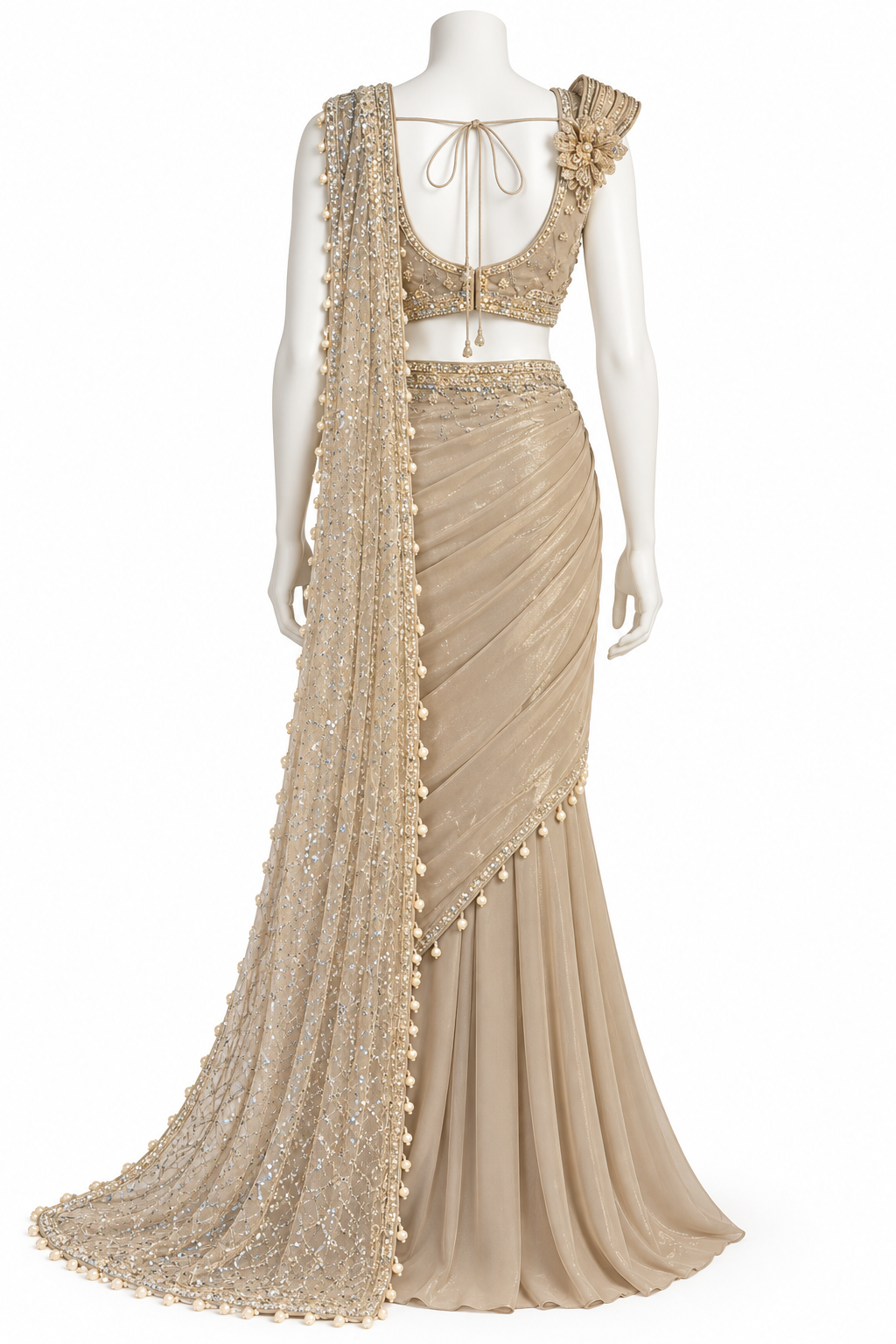A beige embellished lehenga choli set displayed on a white mannequin against a white background. The set features a heavily embroidered choli with a tie-neck and floral shoulder detail, a draped skirt, and a long sheer dupatta with gold beadwork and tassels.