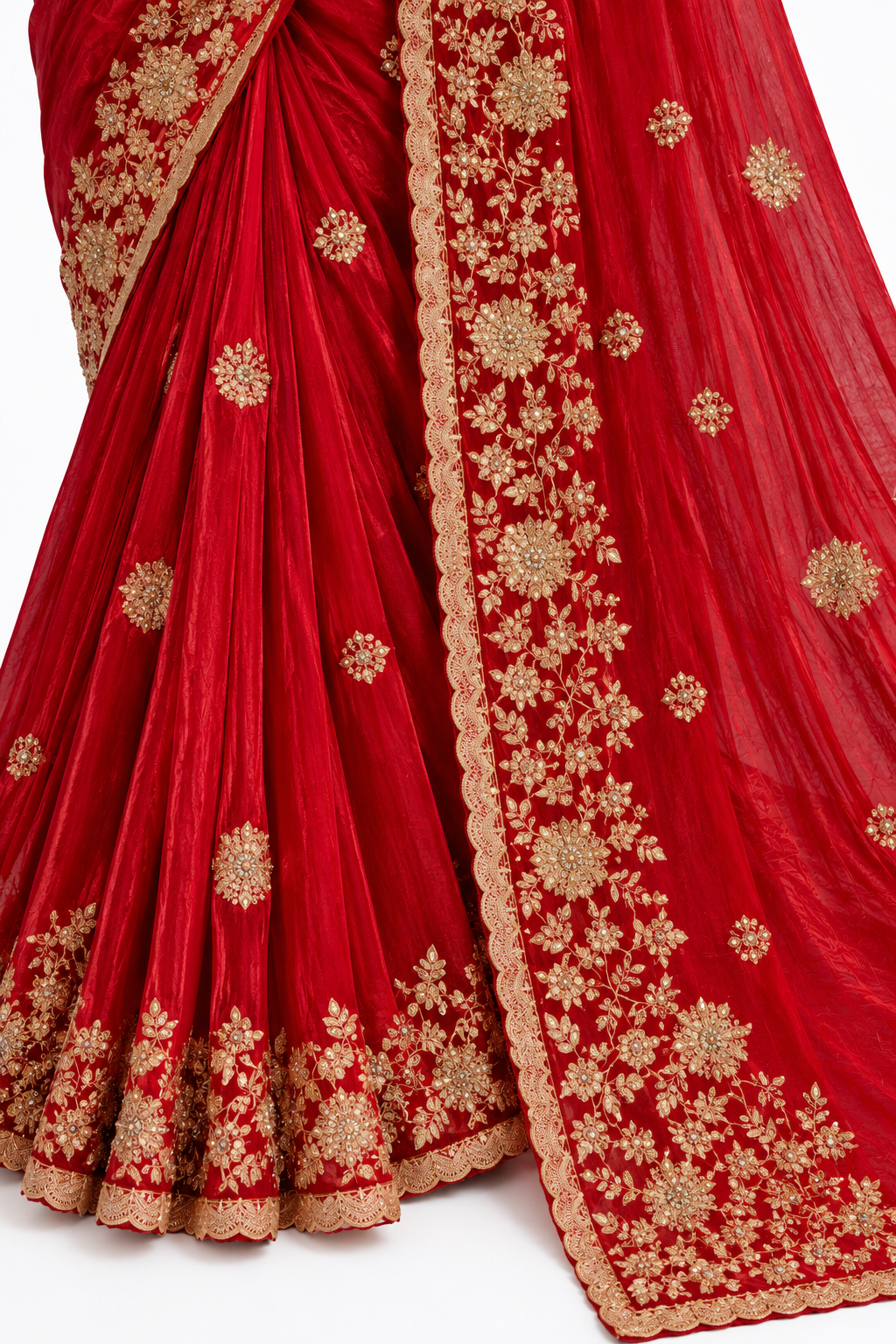 A close-up of a red draped fabric garment, likely a saree or lehenga, featuring intricate gold floral embroidery and a scalloped border, laid out against a white background.