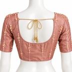A dusty rose linen blouse with gold zari embroidery and pink bead details, shown from the back on a white mannequin. The back features a square cutout with a decorative gold rope tie bow.