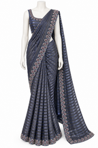 A dark gray-blue saree with a matching sleeveless blouse, displayed on a white mannequin. The fabric features a subtle striped pattern and a prominent geometric border design in pink, gold, and white.