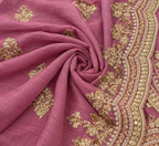 A close-up of a dusty pink fabric, likely a saree or dupatta, featuring intricate gold zari embroidery and beadwork along the border and scattered floral motifs.