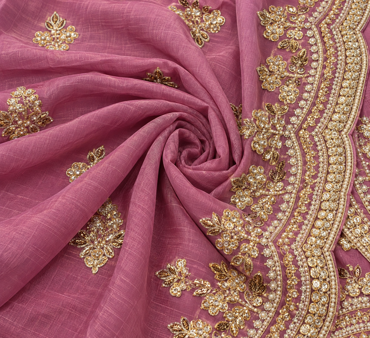A close-up of a dusty pink fabric, likely a saree or dupatta, featuring intricate gold zari embroidery and beadwork along the border and scattered floral motifs.
