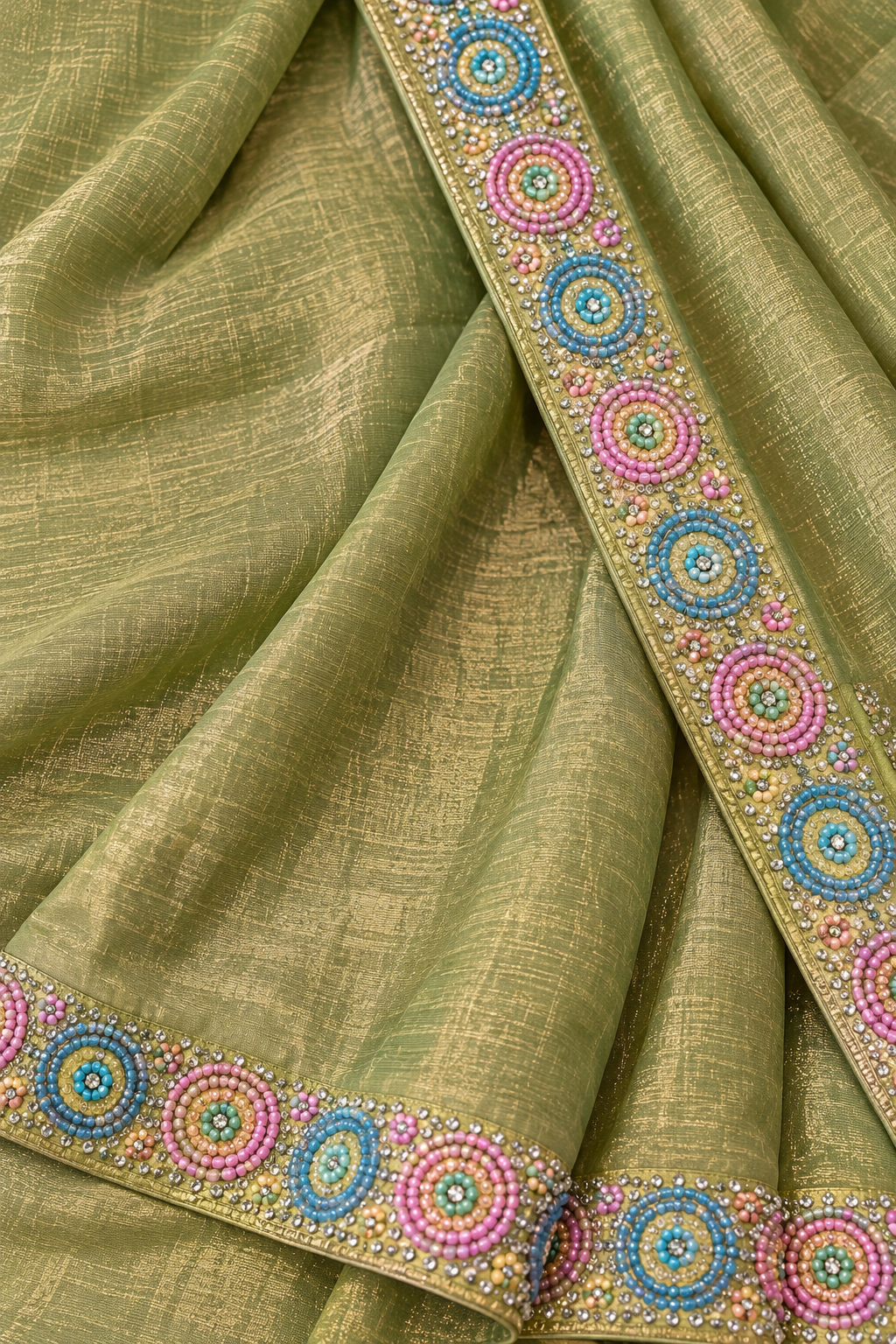 An olive green silk saree with intricate multicolor embroidery on the border, featuring circular patterns in pink, blue, and yellow.