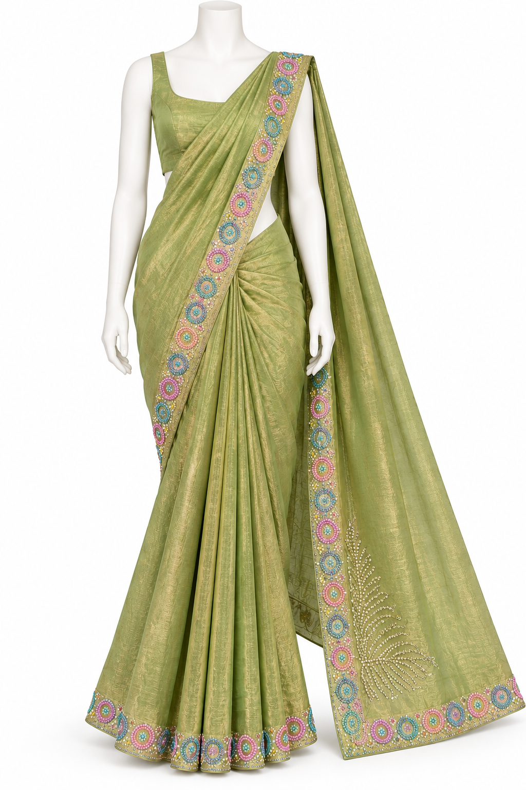 A light olive green saree with a matching sleeveless blouse, displayed on a white mannequin. The saree features a shimmering metallic texture, a multicolor floral patterned border, and a matching embroidered border on the pallu.