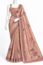 A peach-pink metallic saree with dark brown floral embroidery and border detailing, displayed on a white mannequin against a plain white background.