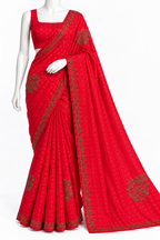 A bright red cotton saree with a matching sleeveless blouse, displayed on a white mannequin. The saree features a subtle woven pattern and detailed gold zari border and floral motifs.