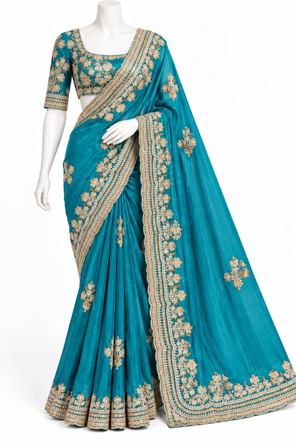 A teal blue saree with intricate gold floral embroidery and a wide gold border, displayed on a white mannequin against a plain white background.