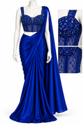A royal blue saree set displayed on a white mannequin, featuring a draped satin saree with a heavily embellished sheer blue and silver beaded blouse, plus a close-up inset showing the blouse details.