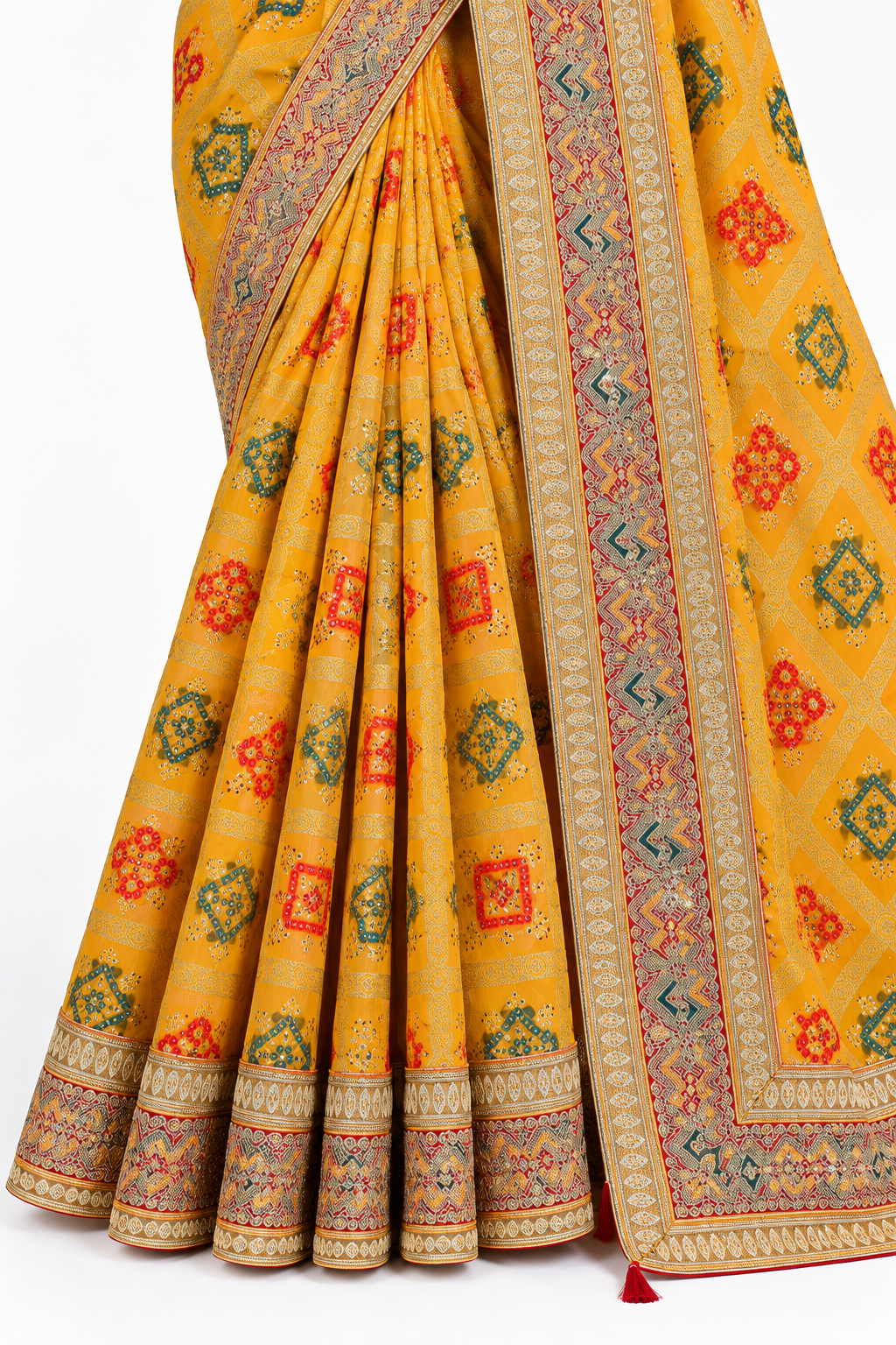 A close-up of a draped mustard yellow fabric with an intricate multicolor pattern of red, green, and orange floral motifs, featuring detailed borders.
