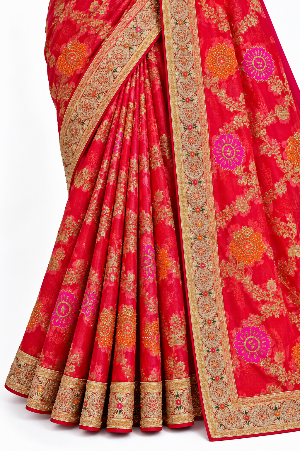 A close-up of a red sari with intricate gold, orange, and pink floral patterns and detailed gold borders, draped elegantly against a plain white background.
