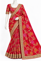 A red flared saree with intricate gold, orange, and pink floral patterns and a wide gold border, displayed on a white mannequin against a plain white background.