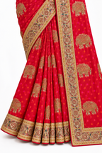 A close-up of a red saree with gold and beige elephant motifs and ornate borders, shown against a plain white background.