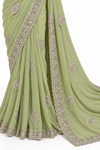 A sage green georgette saree with intricate silver and gold embroidery, shown draped elegantly against a plain white background.