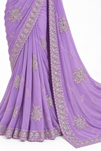A lavender purple saree with intricate silver and gold floral embroidery and border detailing, draped elegantly against a plain white background.