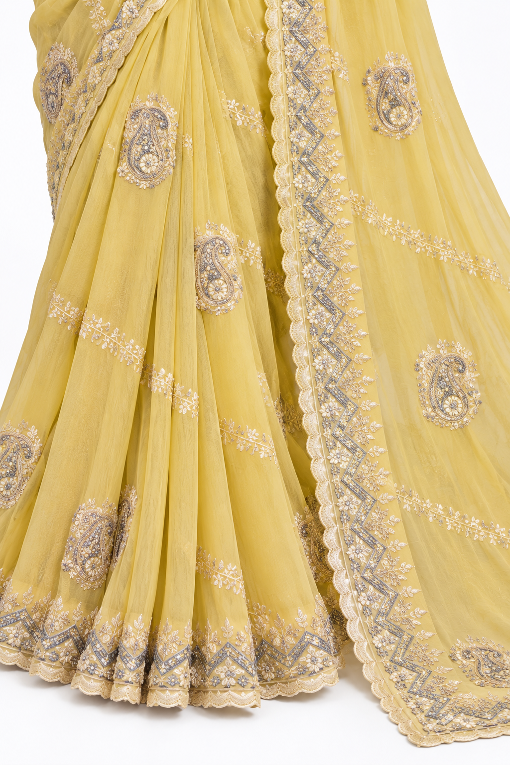 A close-up of a yellow saree with intricate silver and gold embroidery, featuring paisley motifs and a decorative scalloped border.