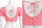 Pink short-sleeve blouse with a square neckline, tie-back bow detail, and subtle floral embroidery, shown on a white mannequin with a close-up inset of the back design.
