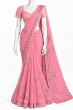 A pink georgette saree with a matching short-sleeve blouse, displayed on a white mannequin. The saree features silver and gold embroidery along the border and scattered motifs on the fabric.