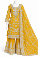 A yellow traditional three-piece outfit displayed on a white mannequin against a white background. The set includes a long-sleeved embroidered kurta, matching wide-leg pants, and a draped dupatta with detailed white embroidery.
