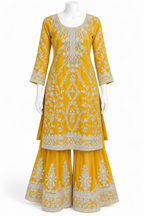 A yellow three-piece salwar kameez suit set displayed on a white mannequin. The set includes a long kurta with intricate white floral embroidery, matching wide flared pants, and a coordinating inner skirt.