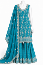 A turquoise blue traditional Indian outfit displayed on a white mannequin, featuring a heavily embroidered sleeveless kurta, matching flared pants, and a coordinating dupatta with intricate silver and gold detailing.