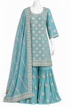 A three-piece traditional outfit displayed on a white mannequin, featuring a turquoise blue kurta and flared sharara pants with beige floral embroidery, accompanied by a matching sheer dupatta.