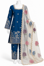 A three-piece Indian ethnic suit set displayed on a white mannequin. The set includes a royal blue kurta with gold floral embroidery, matching blue trousers, and a sheer off-white dupatta decorated with pink, purple, and blue floral embroidery and gold borders.