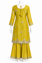A yellow three-piece traditional Indian outfit displayed on a white mannequin, featuring a long kurta with silver floral embroidery, matching pleated pants, and a tie-neck detail.