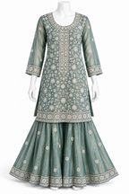 A three-piece traditional Indian outfit displayed on a white mannequin, featuring a dusty teal-green kurta with intricate white floral embroidery, a matching flared skirt, and a coordinating belt.