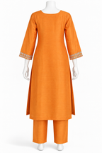 An orange three-piece kurta set displayed on a white mannequin against a plain white background. The set includes a long-sleeved kurta with decorative embroidered cuffs, matching straight trousers, and a coordinating belt.