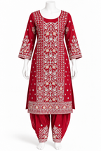 A red Indian ethnic suit set displayed on a white mannequin, featuring a heavily embroidered kurta with matching patola-style pants. The embroidery is detailed in white and gold, showcasing intricate floral and geometric patterns.