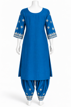 A royal blue kurta set displayed on a white mannequin, featuring a straight-cut tunic with three-quarter sleeves and white floral embroidery at the sleeve cuffs, paired with matching patterned patola-style pants.