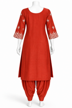 A red kurta and pant set displayed on a white mannequin against a plain white background. The kurta has three-quarter sleeves with white floral embroidery at the cuffs, and the matching pants are gathered at the ankles.