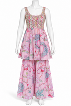 A sleeveless, tiered maxi dress displayed on a white mannequin. The dress features a light pink base with a vibrant floral and butterfly pattern in shades of blue, green, and red, with a heavily embroidered bodice in pink, gold, and green.